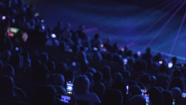 A crowded theater audience filming a live stage event with smartphones in dim lighting.