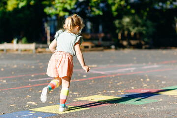 Cute little toddler girl playing hopscotch game drawn with colorful chalks on asphalt. Little...