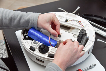 A close-up of a man's hands connecting the new lithium-ion battery inside a robotic vacuum cleaner....