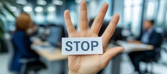 Fototapeta premium Woman s Hand Displaying STOP Sign in Busy Office Environment, Shallow Depth of Field