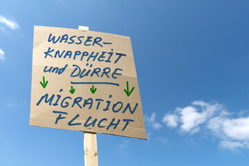 Kartonschild mit der Devise; Wasserknappheit und Dürre führen zu Migration und Flucht
