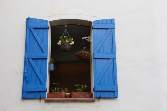French village house open window with blue wooden shutters and hanging flower pots