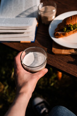 Fototapeta premium woman holding a glass cup of cappuccino latte on a background of croissants with filling in a cafe on the street, French lunch, fast healthy food, pastries, coffee at sunset, wooden background