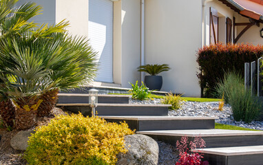 Charmant petit jardin paysagé et ses plantes fleuries au pied d'une maison au printemps.