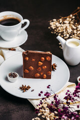 Coffee in a white cup with chocolate, flowers on a dark background, flatlay, chocolate with whole hazelnuts, handmade candies, coffee with milk, exquisite dessert