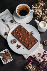 Coffee in a white cup with chocolate, flowers on a dark background, flatlay, chocolate with whole hazelnuts, handmade candies, coffee with milk, exquisite dessert