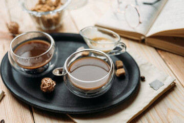 Coffee in glass cup on wooden background, espresso coffee in double-bottomed glass cups, cane sugar, open book, coffee on a black tray, lunch break, coffee still life close-up