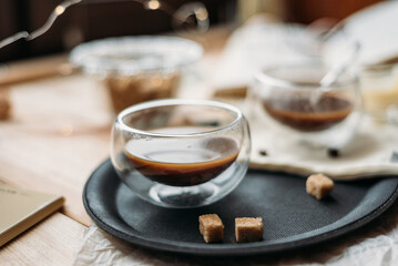 Coffee in glass cup on wooden background, espresso coffee in double-bottomed glass cups, cane sugar, open book, coffee on a black tray, lunch break, coffee still life close-up
