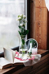 a bouquet of white flowers in a tall glass vase on a wooden windowsill, an open book nearby, a silk pink ribbon, reading glasses, a gift for a woman, a spring still life, flowers in the room