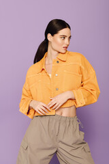 Stylish young woman posing in vibrant orange jacket against a purple backdrop