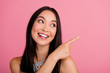 Joyful young woman in stylish summer top points excitedly with a smile against a pink background