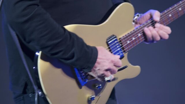 Close-up of a musician playing a gold electric guitar, showcasing their hands and the instrument during a live music performance. Suitable for themes of music, performance, and instrumental artistry.