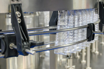 The  empty drinking water bottles  hanging on the overhead conveyor belt for filling process.