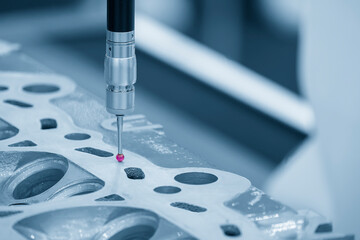 The CMM machine measuring the aluminum cylinder head parts in the light blue scene.