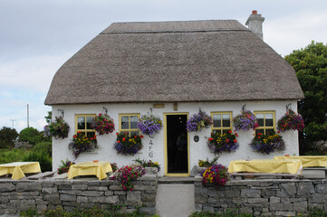 Colorful hanging flower baskets on a white wall of a cafe on the island of Inishmore, one of...