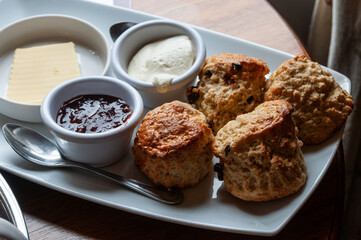 Plate of freshly baked scone pastries, jam, butter and clotted cream.