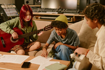 Male member of teen band reading lyrics of song while his female guitarists looking at text and trying to come up with melody