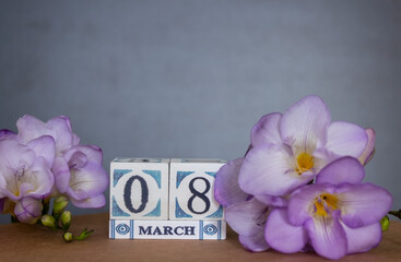 Concept of greeting card on March 8 International Women's day with wooden calendar decorated with freesia flower and copy space.