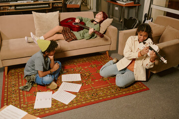 High angle shot of biracial teen band having creative crisis, two members sitting at carpet trying...
