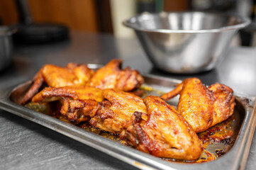 A tray of freshly cooked chicken wings, golden and crispy, served in a kitchen setting. A mixing bowl in the background adds to the culinary atmosphere, perfect for food-related projects.