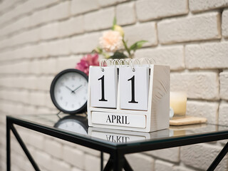 April 11th. wooden calendar on glass table with candle and clock