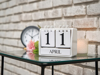 April 11th. wooden calendar on glass table with candle and clock