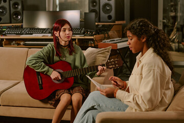 Wide shot of two teen girls sitting at studio fully equipped with modern equipment, guitarists...