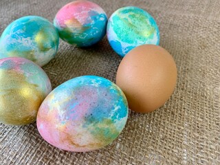 Vibrantly decorated Easter eggs in various colors are displayed in a circular arrangement on a textured burlap surface, capturing a festive spring atmosphere