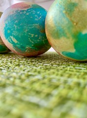Three intricately painted eggs with shades of green and gold are positioned on a lively green textured surface, creating a cheerful atmosphere perfect for spring celebrations