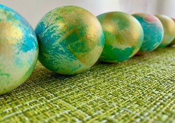 A series of decorative Easter eggs display vibrant colors and unique patterns. They are placed on a green textured cloth, providing a cheerful ambiance suitable for spring celebrations