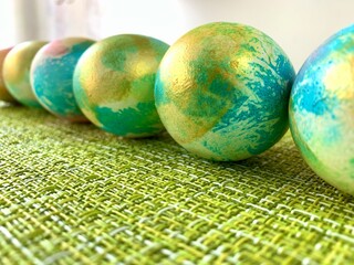 Brightly painted decorative eggs in shades of blue and gold are neatly arranged on a textured green...