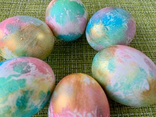 Colorful Easter eggs display a mix of pastel hues and metallic finishes, artfully arranged in a circle on a green surface, perfect for festive decoration