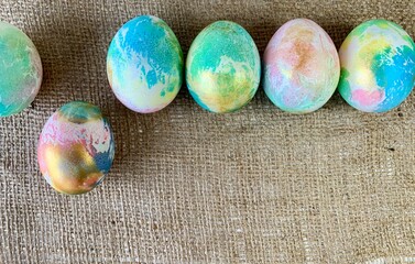 Vibrant Easter eggs showcase a marbled design, placed neatly in a row on a textured burlap surface....