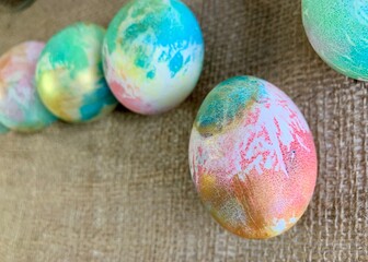 Vibrant eggs in pastel colors are lined up on a textured burlap surface. These decorative eggs showcase artistic patterns and are perfect for springtime festivities