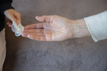 A child's hand holds a damaged pacifier while an adult assists, symbolizing the transition from excessive use to letting go. A touching moment of growth and change.