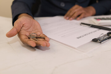 Hand holding keys over paperwork on a desk