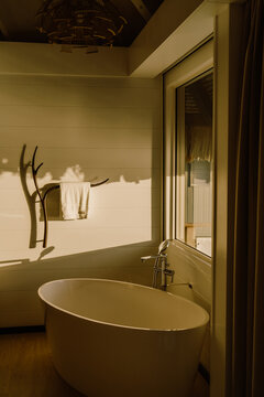 A luxurious bathroom with a freestanding bathtub, bathed in warm golden sunlight. A large window offers a breathtaking ocean view, blending modern elegance with a tropical, nature-inspired ambiance