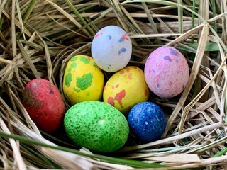 A collection of vibrant, painted eggs nestled together in a natural nest made of straw, symbolizing new life and the arrival of springtime