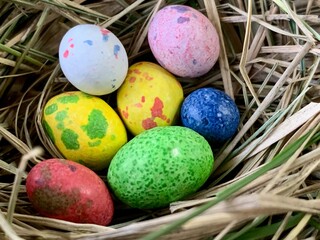 Brightly colored eggs in various shades rest in a cozy nest made of grass, capturing the essence of spring celebrations and traditions