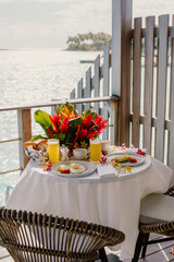 A tropical breakfast setup on a terrace overlooking crystal-clear waters, featuring fresh juice, eggs, pastries, and vibrant red flowers, creating a luxurious and relaxing island dining experience