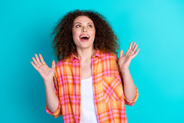 Young woman in a checkered shirt gesturing excitedly against a turquoise background, expressing...