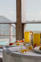 A tropical breakfast setup on a terrace overlooking crystal-clear waters, featuring fresh juice, eggs, pastries, and vibrant red flowers, creating a luxurious and relaxing island dining experience