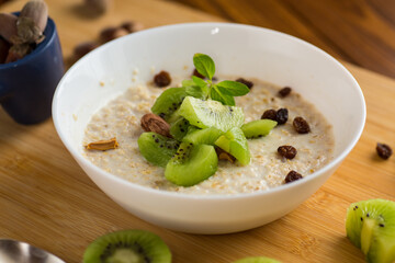 cooked oatmeal with kiwi, honey and nuts in a bowl on a wooden table