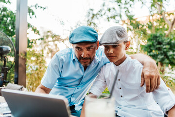 Handsome and happy father and his teenage son sitting in a restaurant and talking.