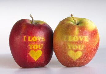 Two apples with ‘I Love You’ written on them, placed on a white background.