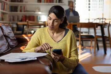 Woman using smartphone while reviewing bills