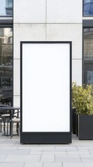 A blank advertising board stands outside a modern building, framed in black, with greenery nearby.