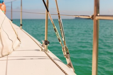 Fototapeta premium A close-up of a sailboat deck with metal rigging, ropes, and turquoise ocean water in the background. The warm sunlight highlights the details, evoking themes of sailing, adventure, and ocean travel