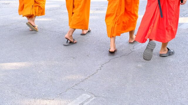 Three monks walk down a street in orange robes. They are barefoot and wearing sandals. Concept of peace and simplicity