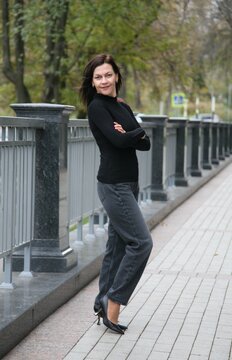 Pretty middle age brunette woman 51+ years old in modern graphite mom jeans poses with crossed arms and looks at the camera